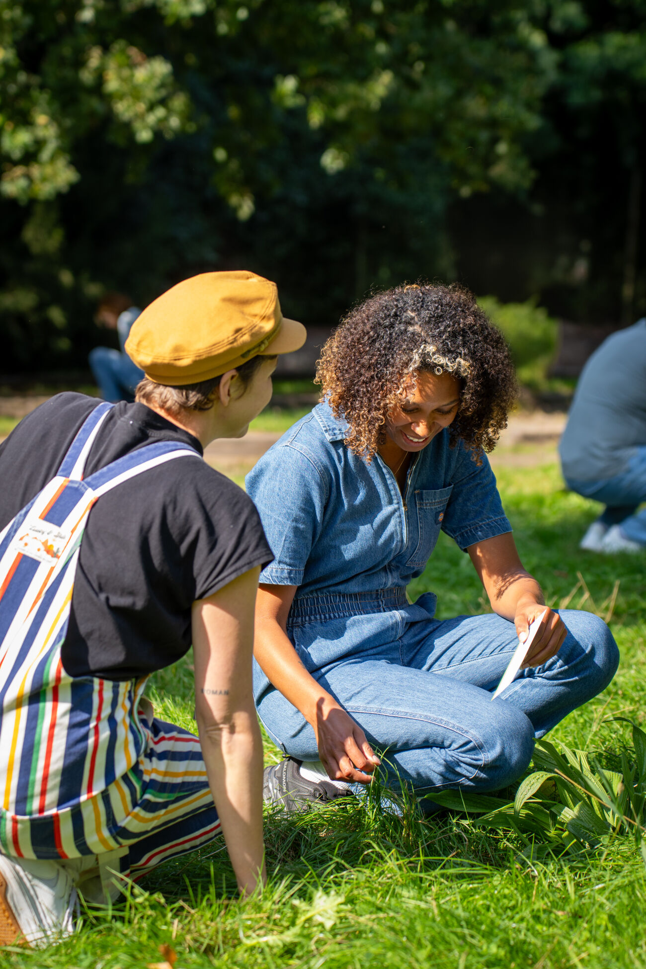 Twee mensen zitten buiten op gras, lachend en pratend met een notitieblok.