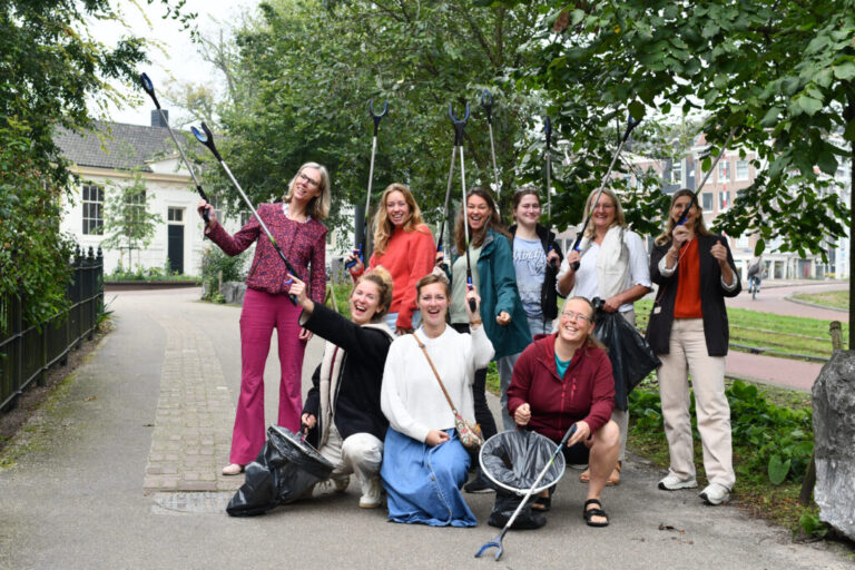 Groep mensen enthousiast poserende met afvalgrijpers in een park.