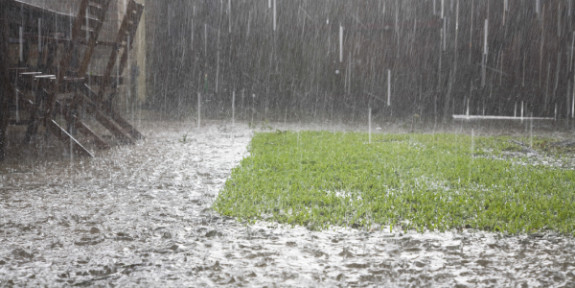 Intense regenval overstroomt een tuin met gras en beklinkerde paden.