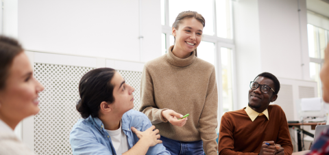 Groep mensen in discussie, vrouw in trui lacht en houdt groen object vast.