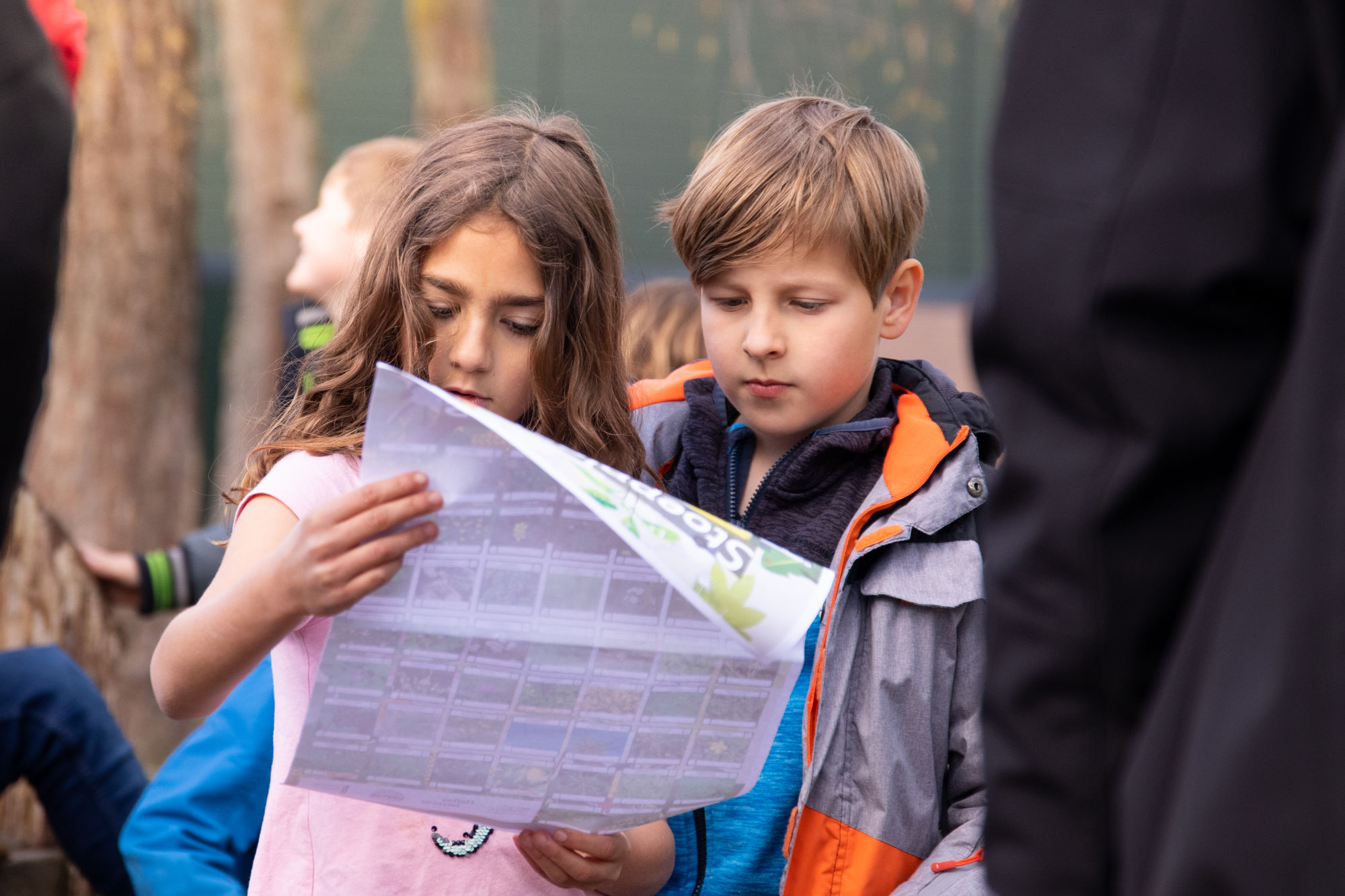 Twee kinderen bekijken samen een grote kaart in een buitenomgeving.