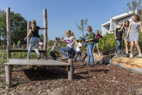 Kinderen spelen buiten op een houten speeltoestel en stenen onder een heldere blauwe lucht.