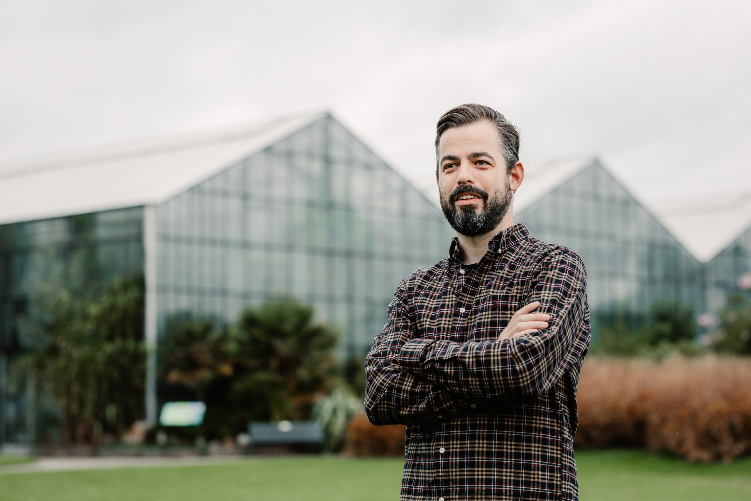 Man met baard staat voor grote glazen kas.