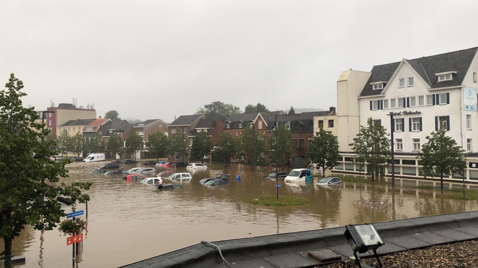 Overstroomde straat met ondergelopen auto's en gebouwen op een bewolkte dag.