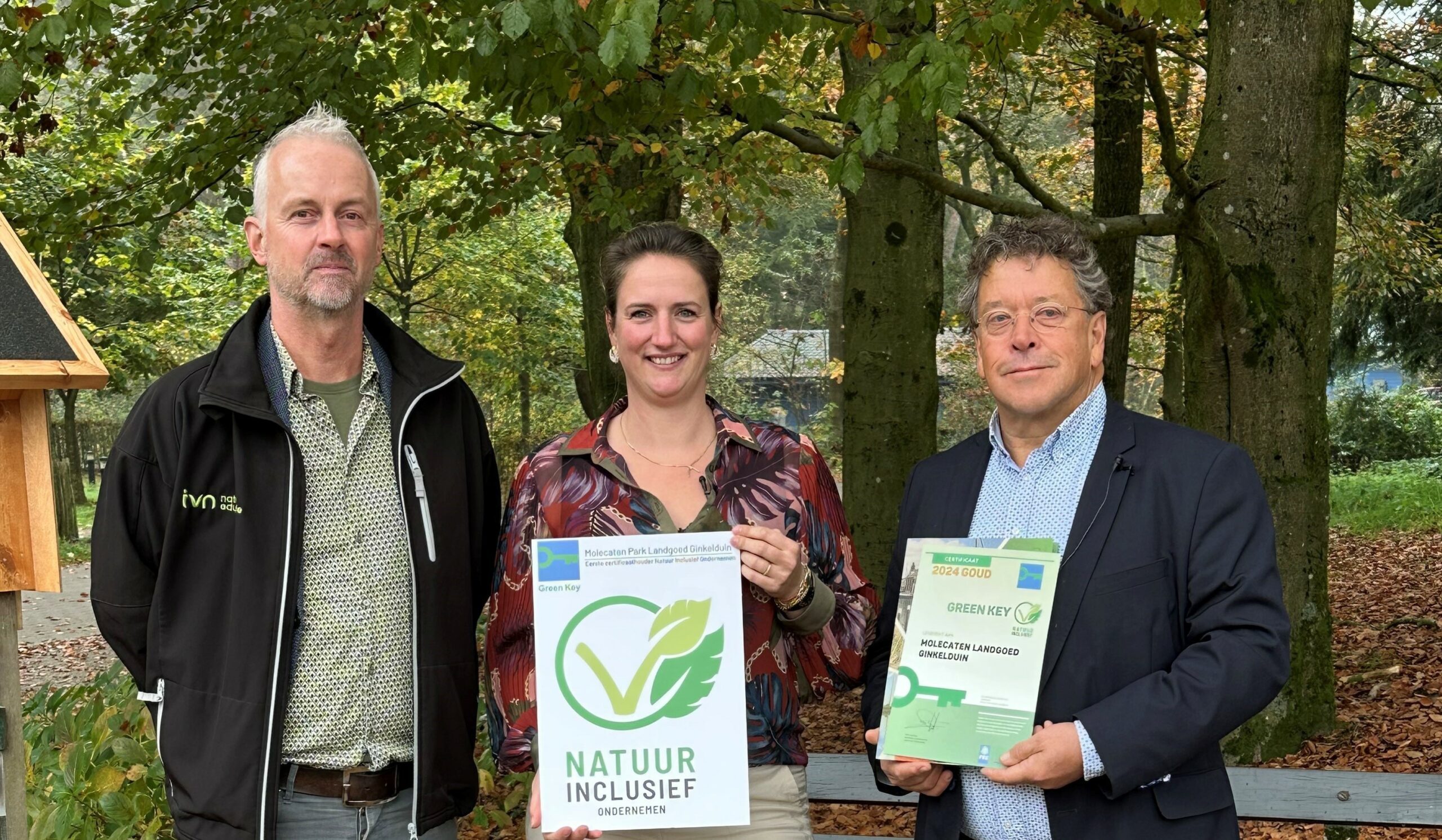 Drie mensen poseren buiten met Green Key certificaten in een bosrijke omgeving.