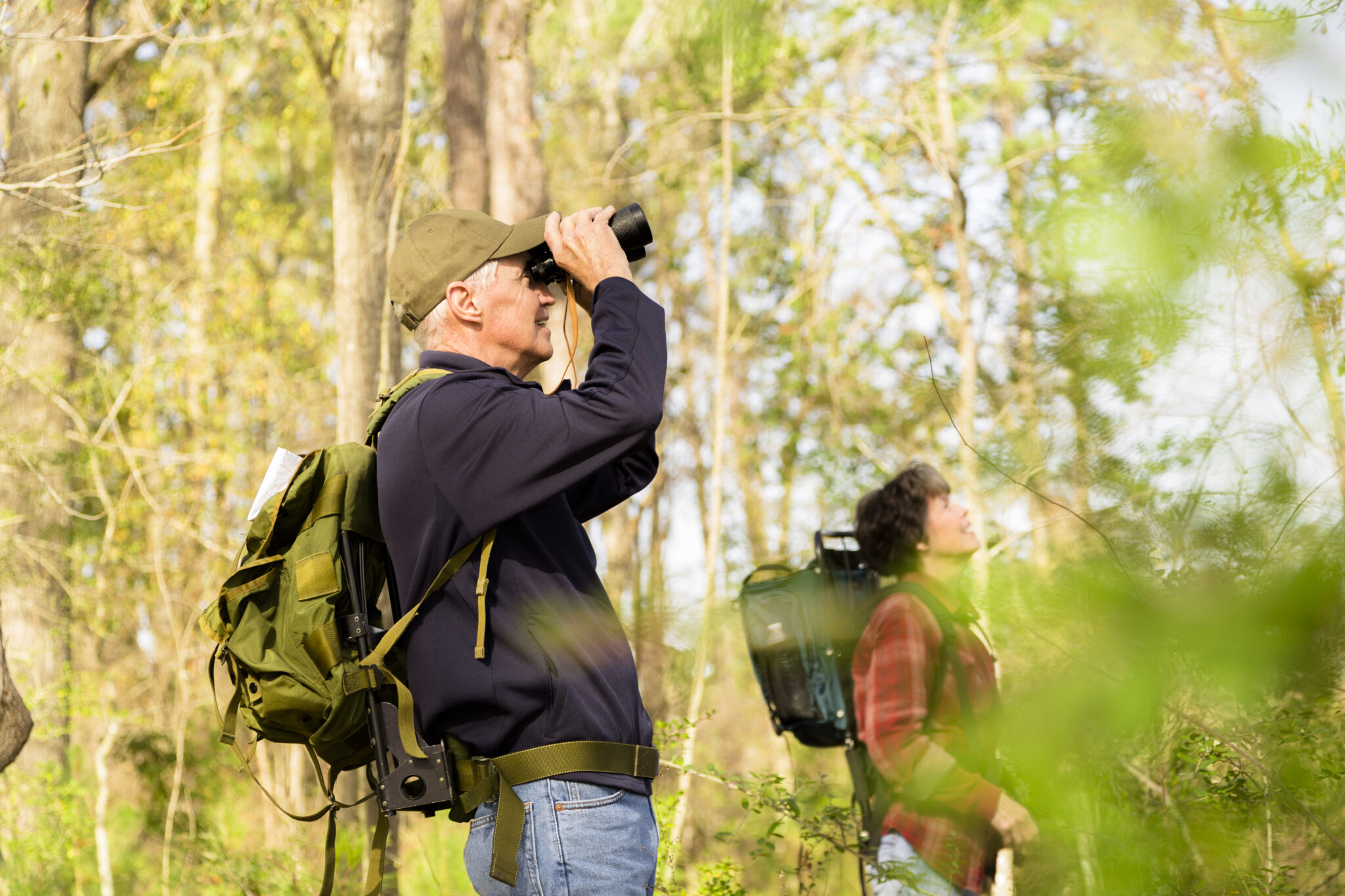 Twee mensen vogels observeren in een bos, met verrekijkers en rugzakken.