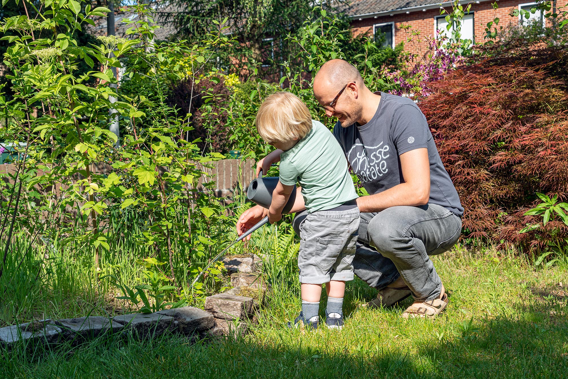 Vader helpt kind planten water geven in zonnige tuin.