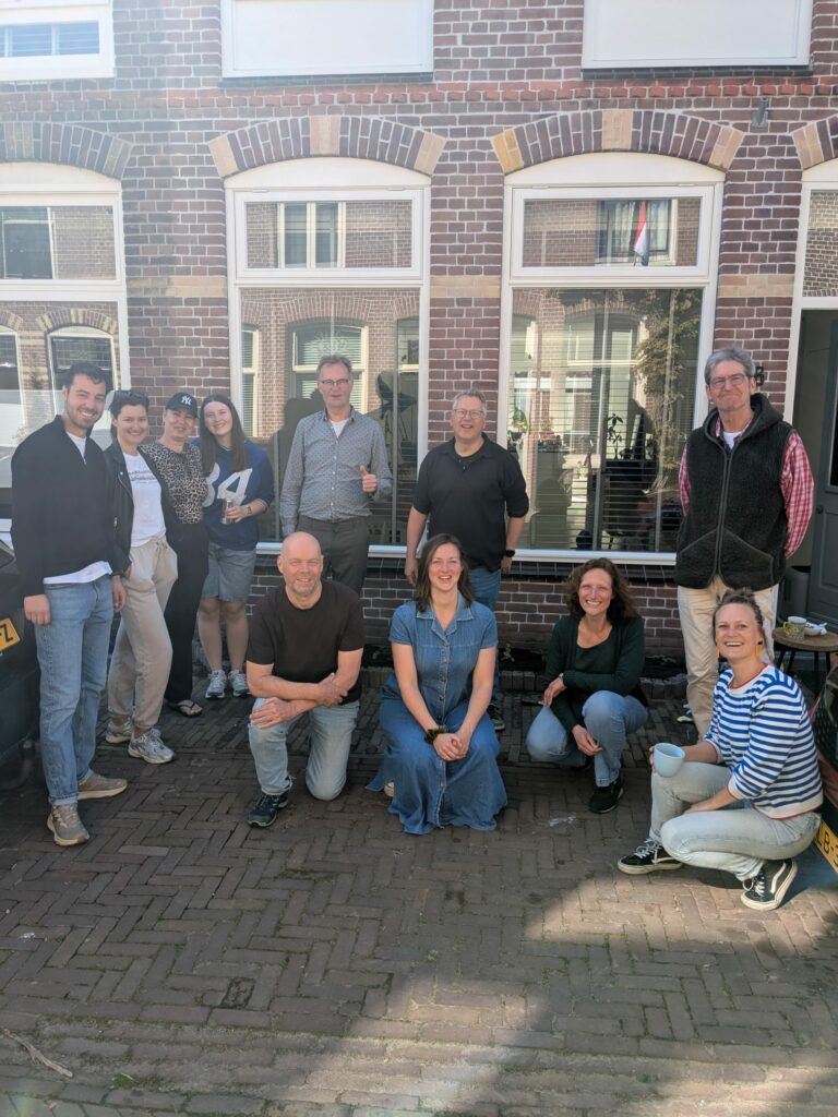 Een groep mensen poseert buiten voor een bakstenen gebouw op een zonnige dag.