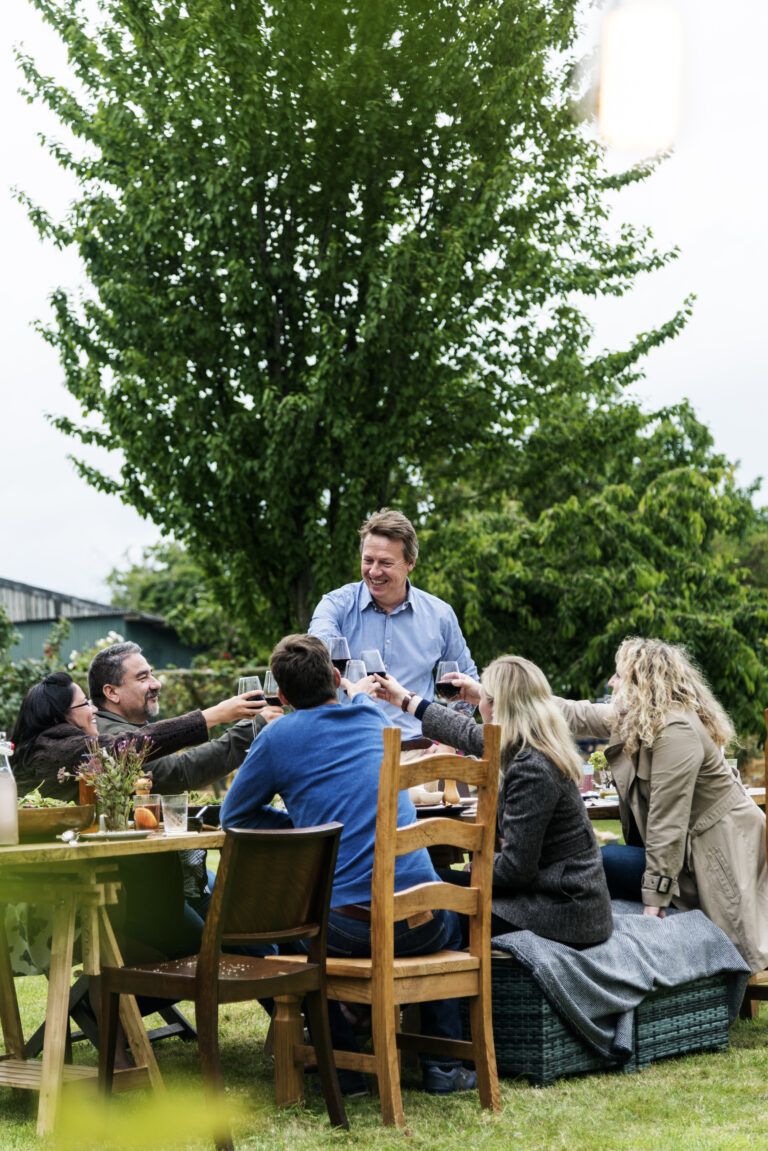Groep mensen in een tuin die samen proosten rond een tafel vol eten.