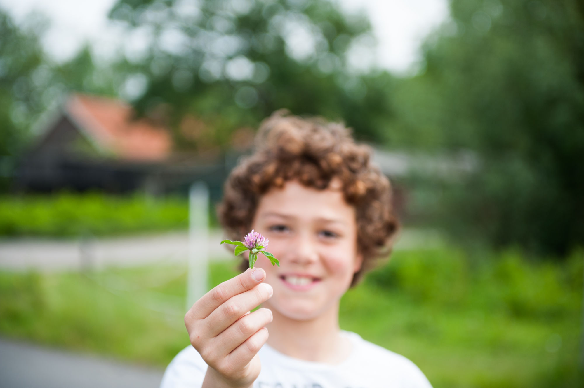 Kind met krullend haar toont een kleine, paarse bloem, onscherpe groene achtergrond.