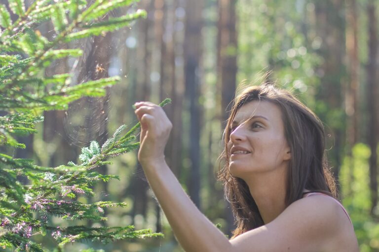 Vrouw bewondert een spinnenweb in een bosrijke omgeving, zonlicht verlicht de scène.