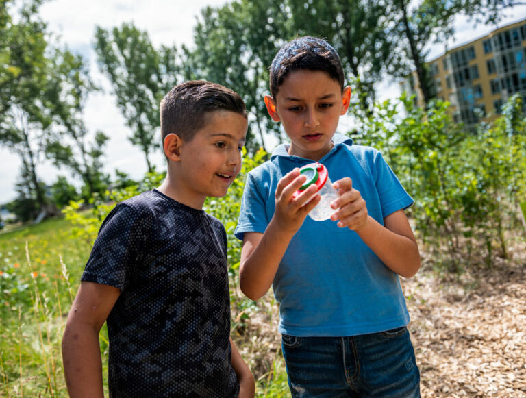 Jongens bestuderen insect in loepbeker in een groen park.