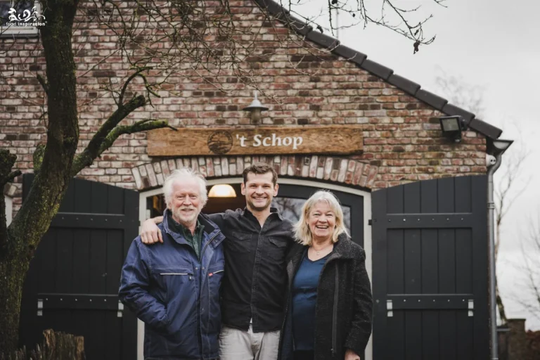Ik weet niet wie dit zijn, maar ik kan je de beschrijving geven! Drie mensen staan lachend voor een bakstenen gebouw met een bord 't Schop.