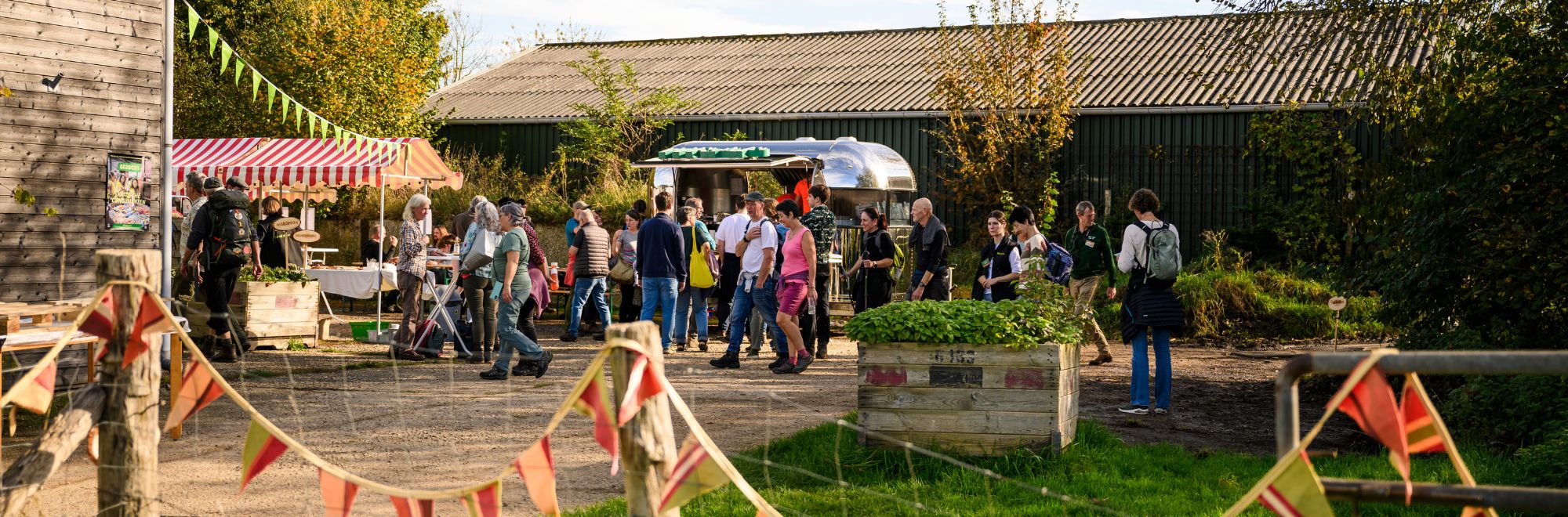 Groep mensen bij marktkraampjes op een buitenevenement met feestvlaggetjes.