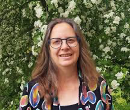 Een persoon met bril staat voor een bloeiende struik met witte bloemen.