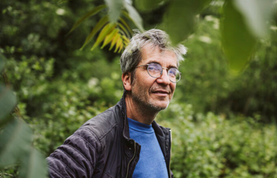 Man buiten in groene tuin, draagt bril en donkerjack.
