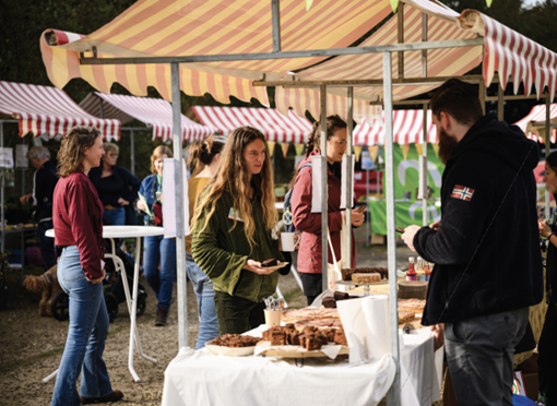 Mensen bij een marktstal met gebakjes onder gestreepte luifels.