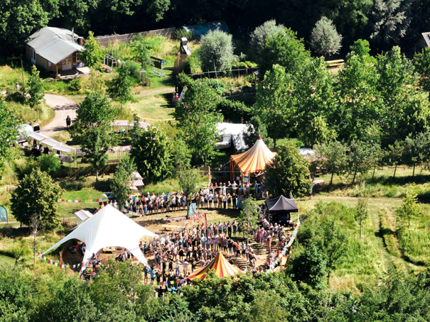 Luchtfoto van een festival met tenten, een menigte en bomen in een groene omgeving.