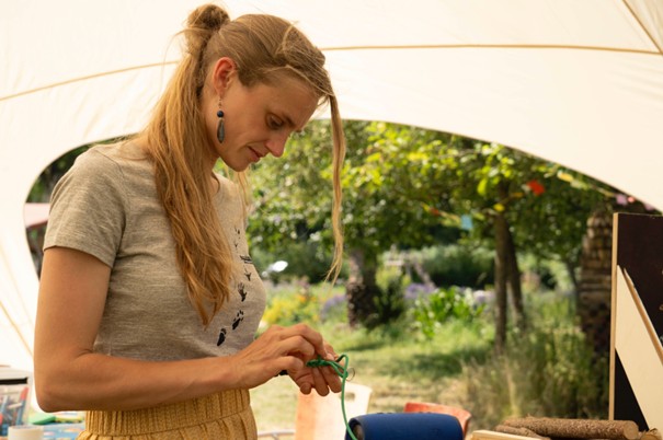 Vrouw knutselt buiten onder een tent, omgeven door groene planten.