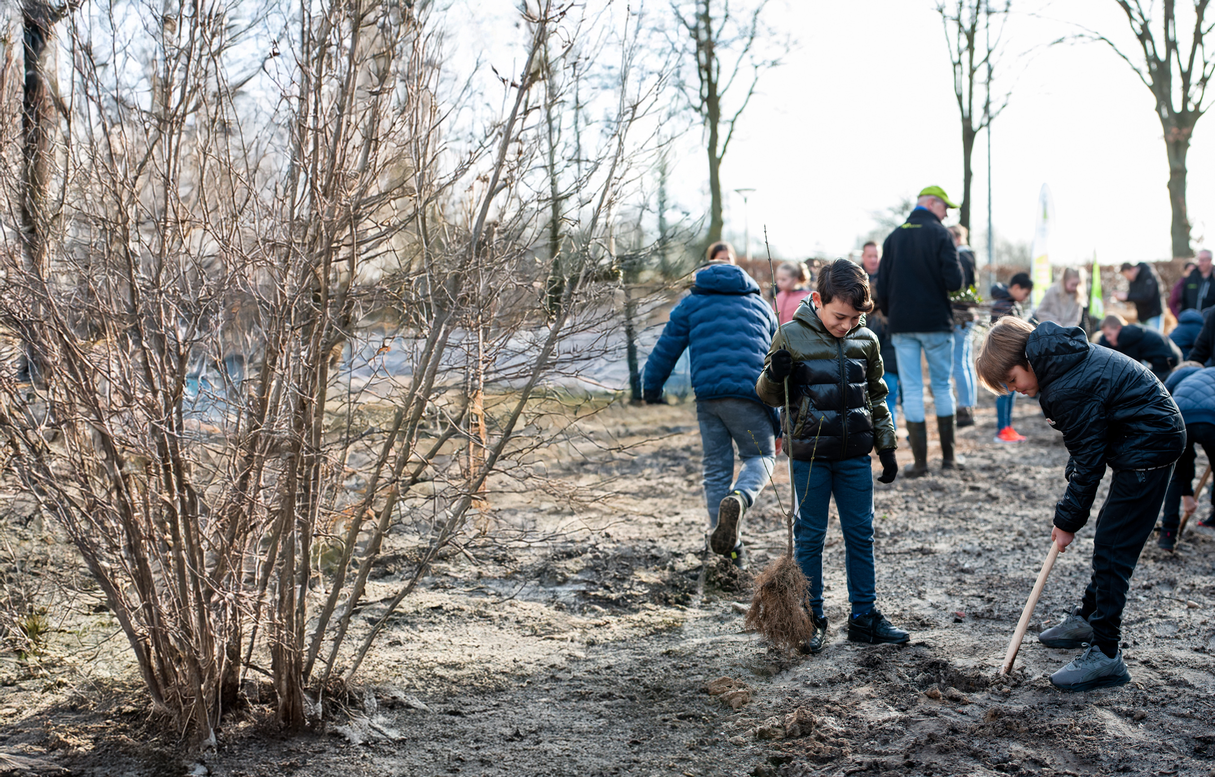 Children plant trees in a muddy field during a community outdoor activity.