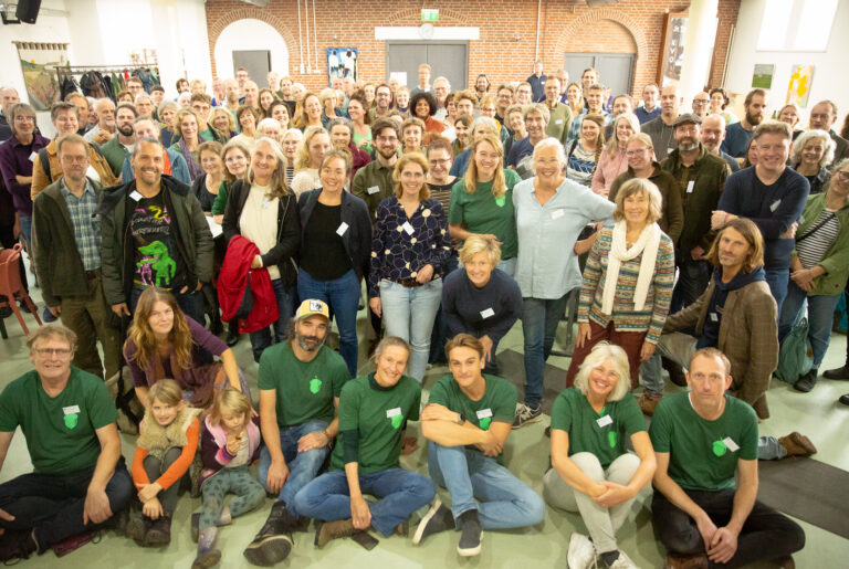 Een grote, diverse groep mensen poseert samen in een zaal.