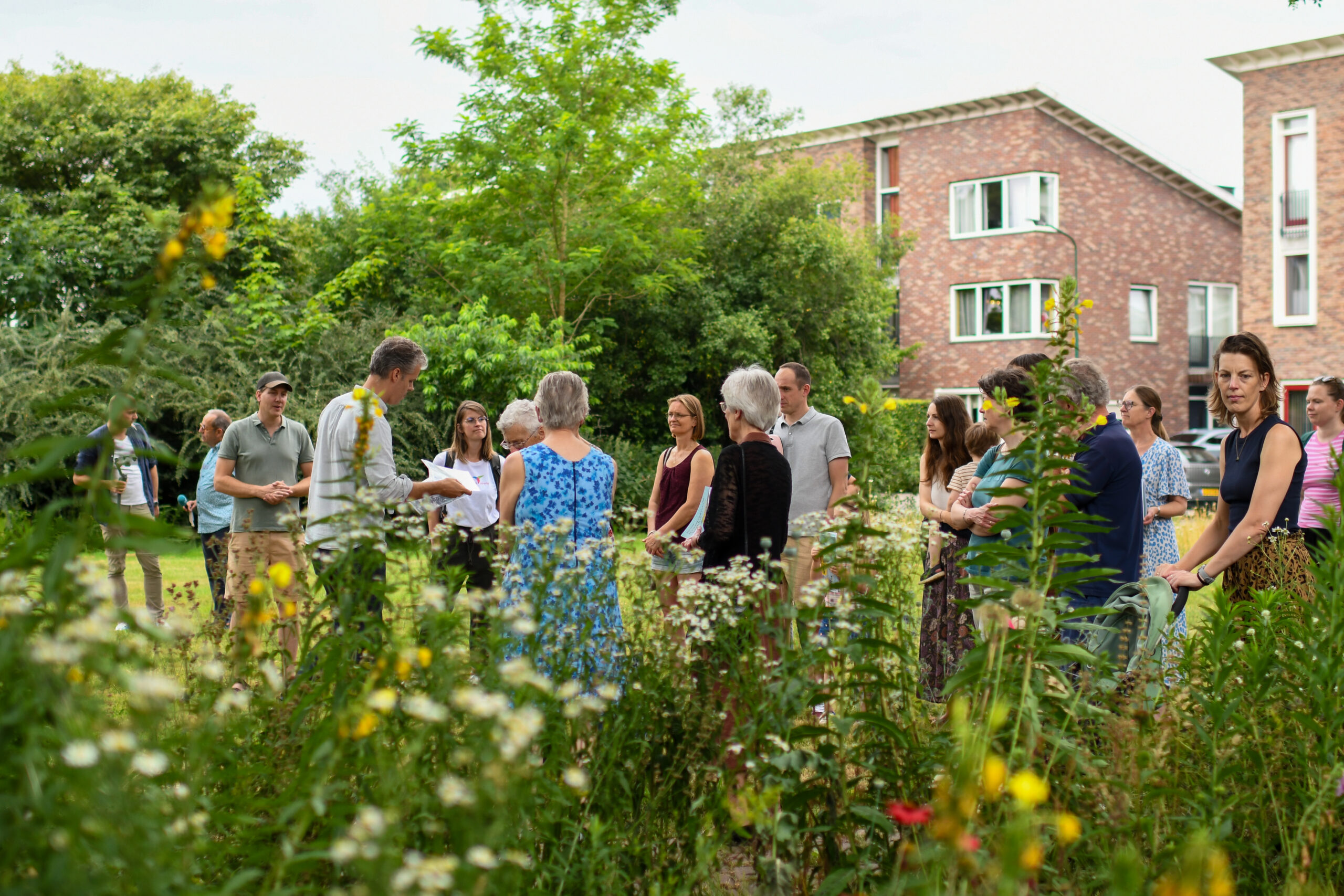 Een groep mensen verzameld in een groene tuin met wilde bloemen.