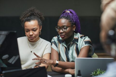Twee vrouwen werken samen aan laptops in een kantooromgeving.