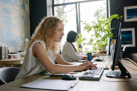 Twee mensen werken aan computerschermen in een licht kantoor met planten en kunst aan de muur.