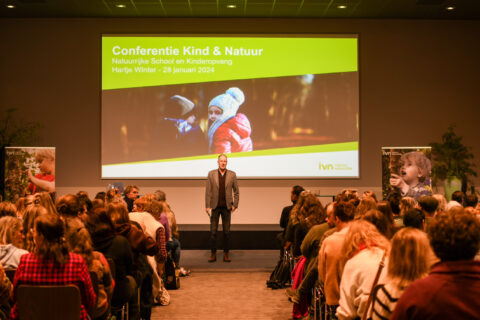 Een spreker presenteert op de conferentie "Kind & Natuur" voor een volle zaal.