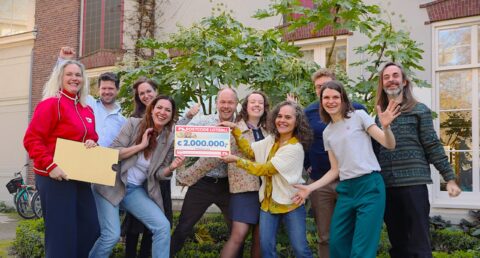 Groep mensen viert winnen van €2.000.000 in de Postcode Loterij, met feestelijke blikken en cheque.