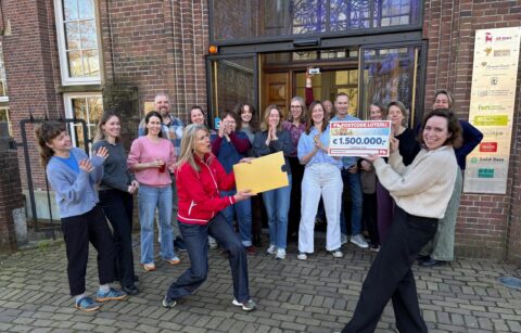 Groep mensen viert een Postcode Loterij-cheque van €1.500.000 voor een gebouw.