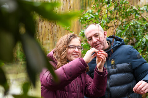 Twee mensen onderzoeken takjes in een groene tuinomgeving.