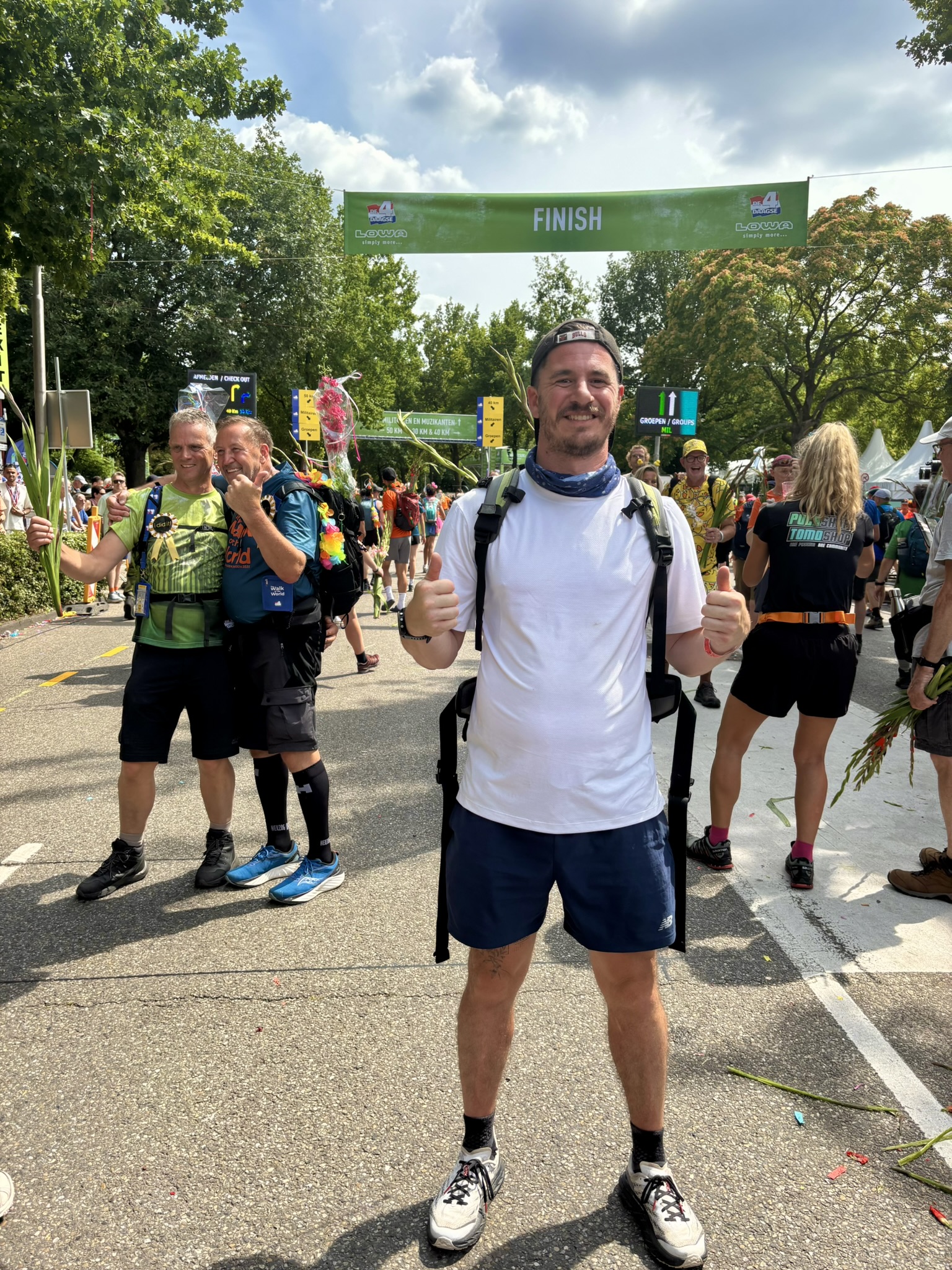 Man bij finishlijn van een wandeltocht, omringd door andere wandelaars en natuuromgeving.