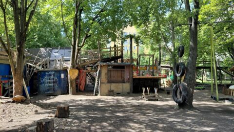Ongestructureerde speeltuin met houten hutten, bomen en autobanden als schommels.