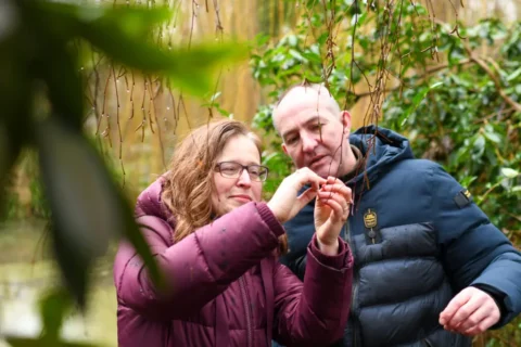 Twee mensen inspecteren een takje in een groene, natuurlijke omgeving.