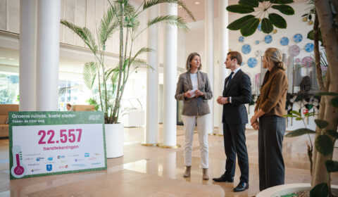 Drie mensen in gesprek naast een bord met "22.557 handtekeningen" over groene steden in een lobby.