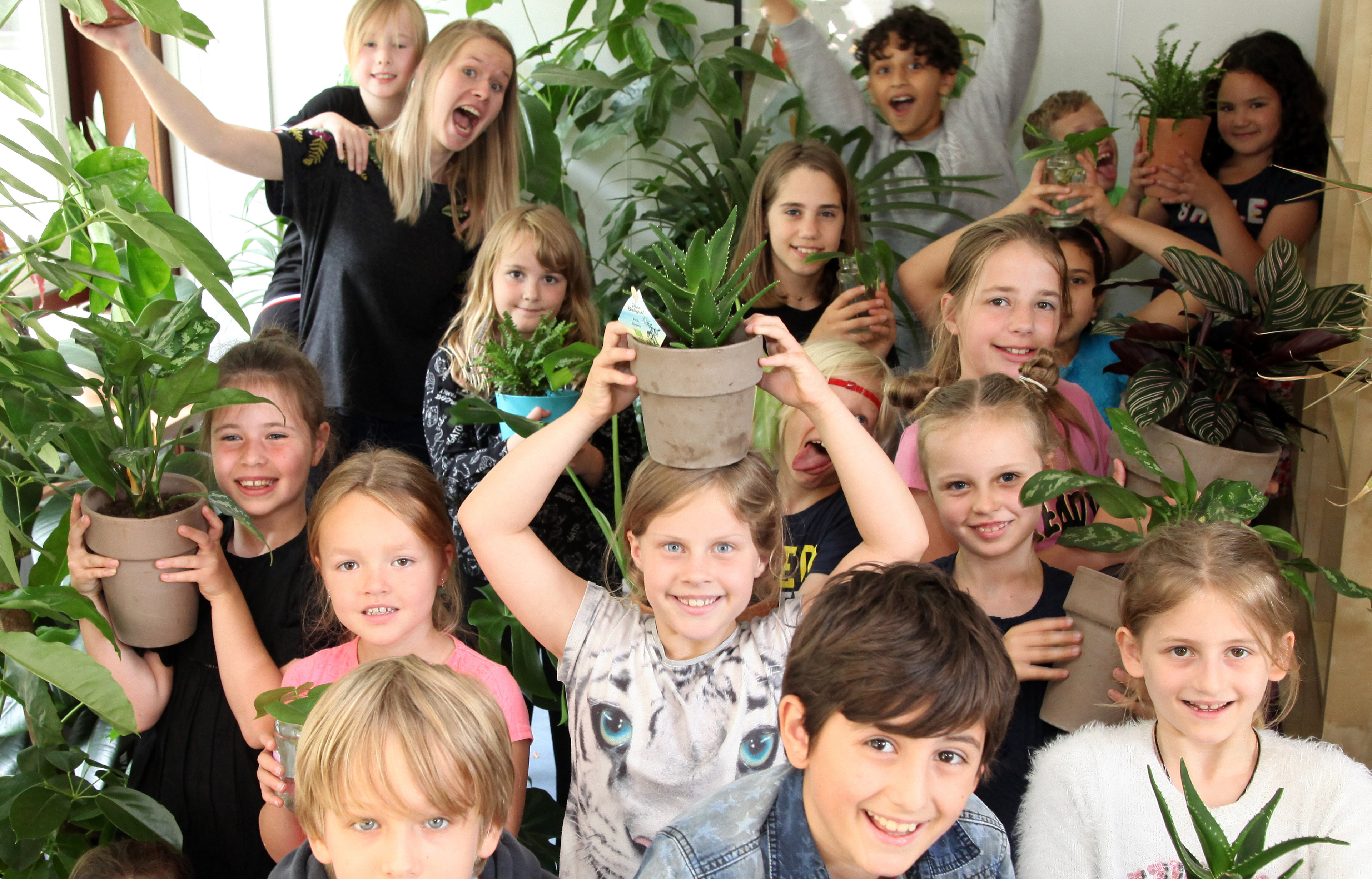 Een groep blije kinderen met kamerplanten in handen, omringd door groen.