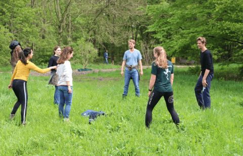 Een groep mensen speelt een spel in een groene weide in het bos.