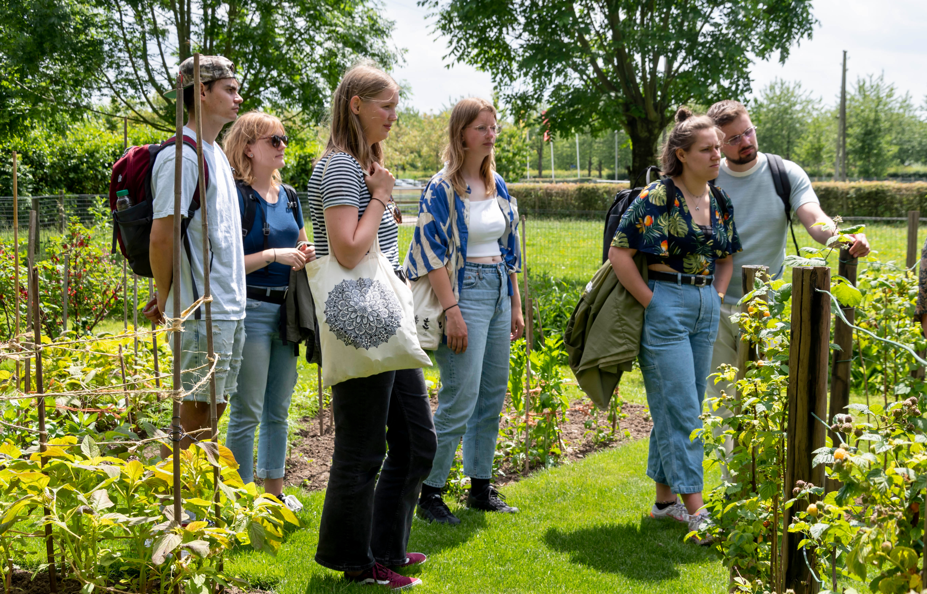 Groep mensen luistert naar een gids in een groene tuinomgeving.