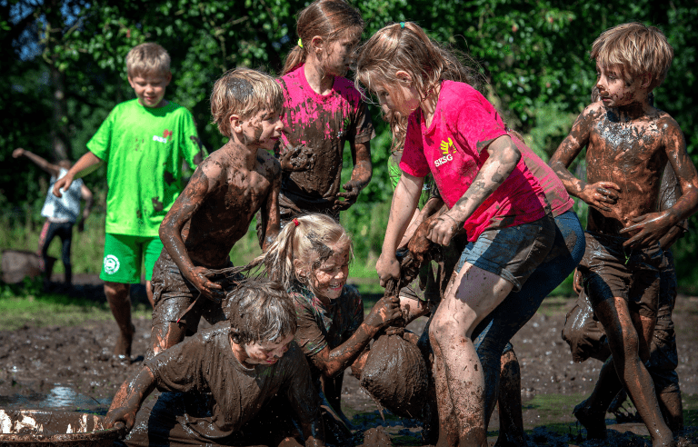 Kinderen spelen lachend in de modder, bedekt met aarde, op een zonnige dag in de buitenlucht.