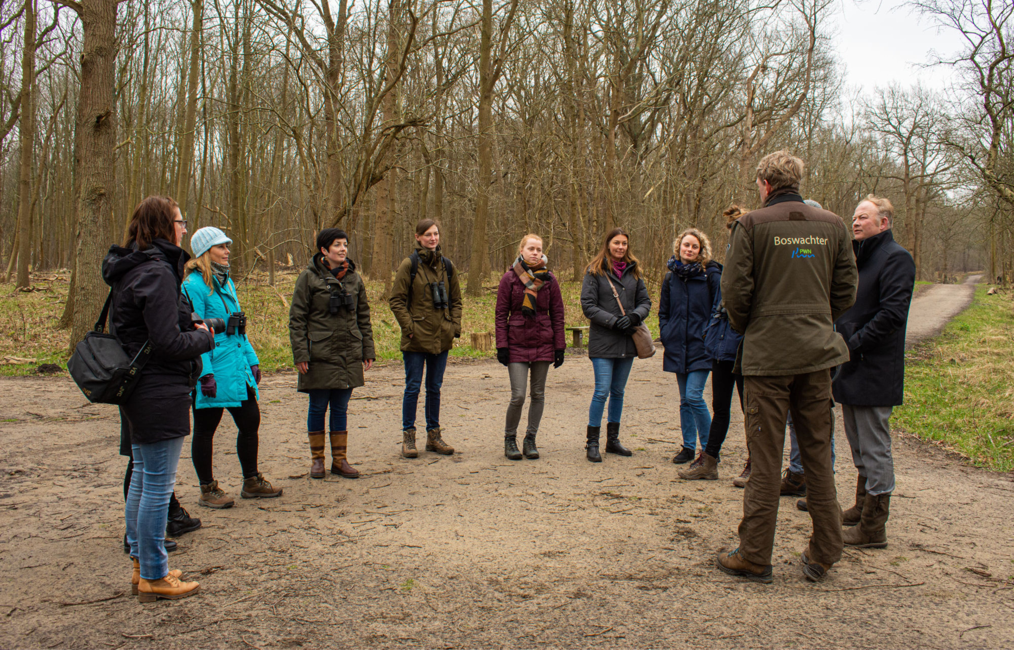 Groep mensen luistert naar een boswachter in een bos tijdens een natuurwandeling.