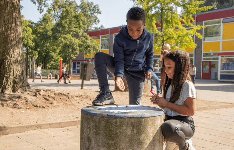 Kinderen spelen een spel op het schoolplein, met dobbelstenen op een betonnen paal.