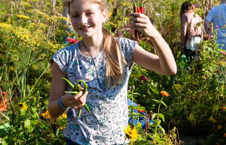 Meisje in bloemenveld houdt pepers vast, genietend van de zon.