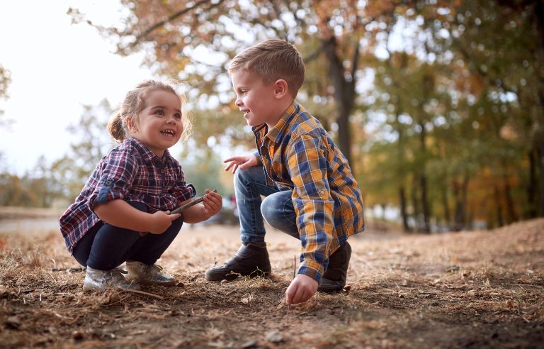 Kinderen spelen samen in een bos, gehurkt op de grond tijdens een herfstdag.