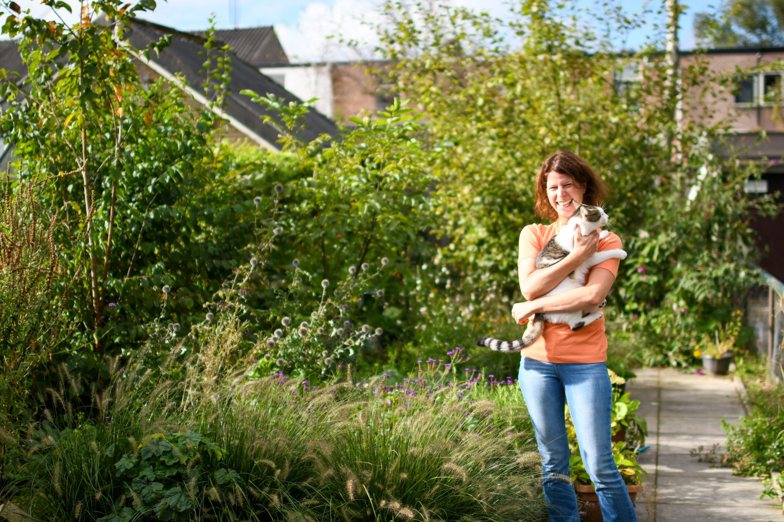 Een vrouw staat in een tuin met veel groen en houdt een kat vast.