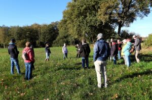 Groep mensen verzameld in een open veld met bomen op de achtergrond, luisterend naar een spreker.