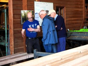 Drie mannen bespreken houtbewerking naast een machine in een werkplaats.