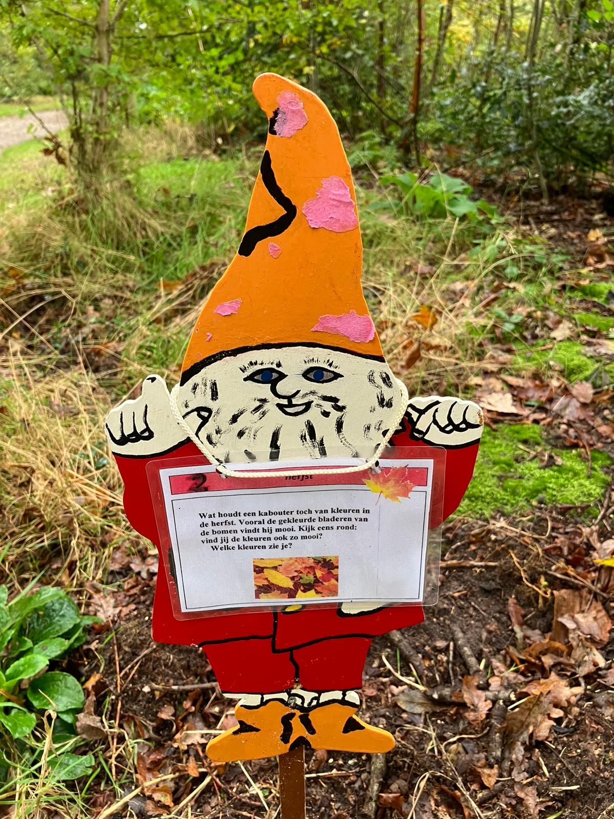 Een houten kabouter in het bos met een informatiekaartje over herfstkleuren.