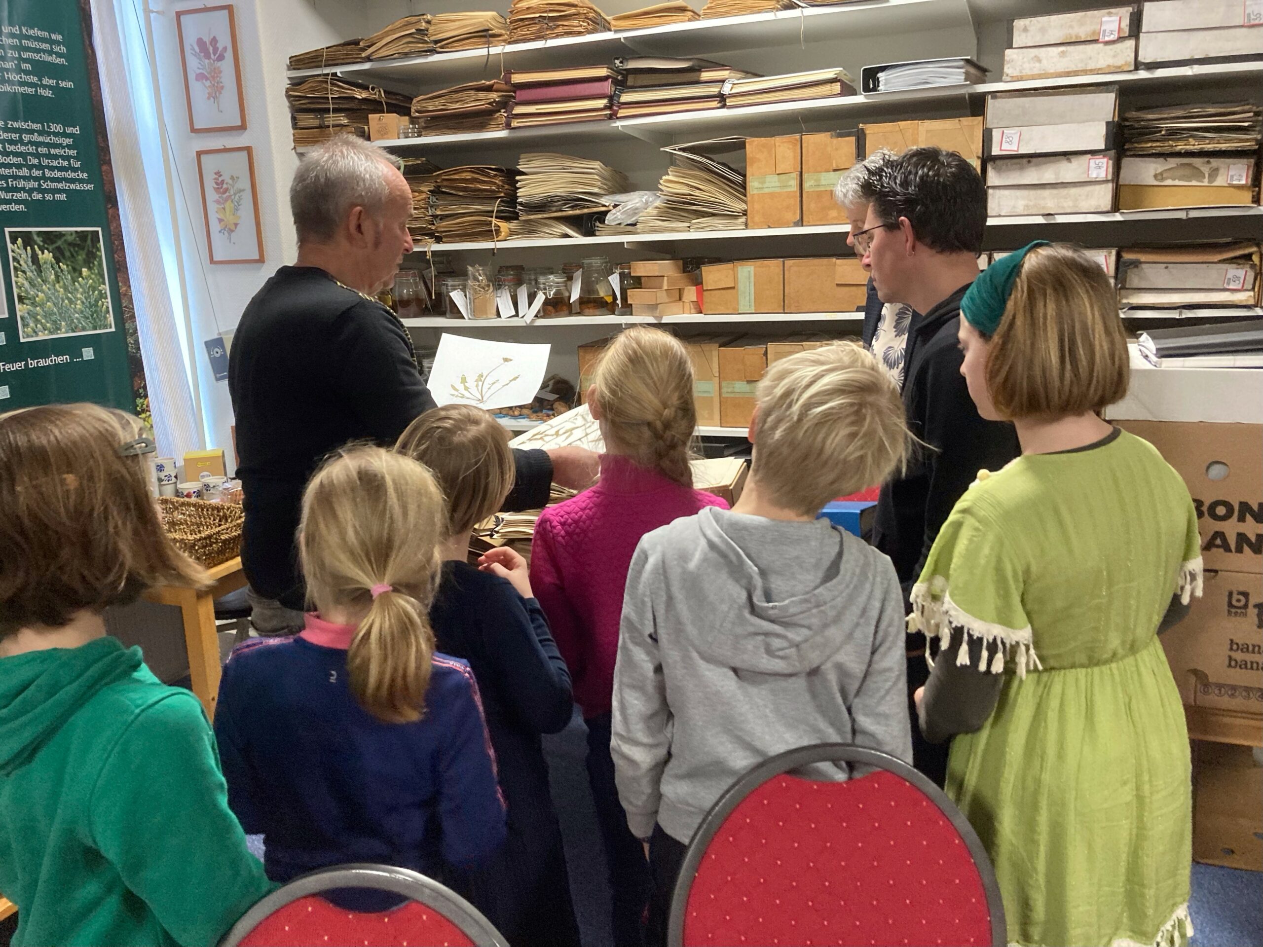 Man toont plant aan kinderen in opslagruimte vol boeken en dozen.