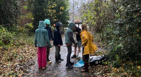 Kinderen in regenjassen verzamelen zich op een bosrijk pad, omgeven door herfstbladeren.